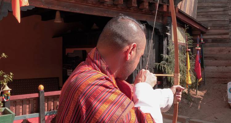 Archer bhoutanais en tenue traditionnelle visant avec un arc en bois sur un terrain de tir extérieur