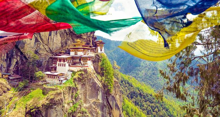 Vue spectaculaire du monastère du Nid du Tigre accroché à une falaise encadré par des drapeaux de prière colorés