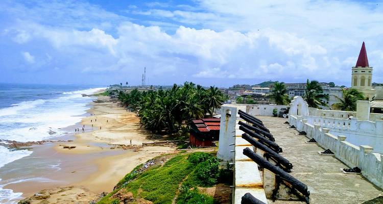Scène côtière avec plage, palmiers et fort historique.