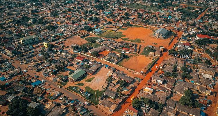 Vue aérienne par drone d'un paysage urbain étendu avec des routes en terre orange et des bâtiments bas et mixtes au Ghana.