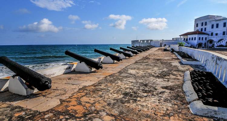Row of historic black cannons overlooking the Atlantic Ocean on the weathered ramparts of Cape Coast Castle.