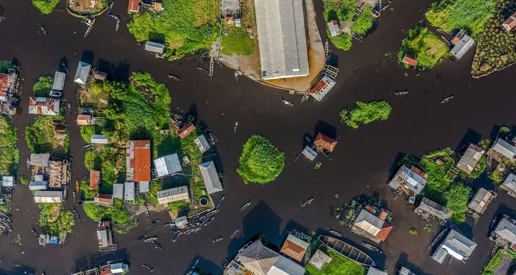 Aerial view of a stilt village with houses and boats scattered across dark water and lush green islets.