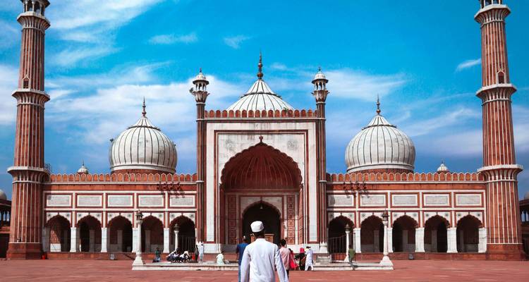 Una persona caminando hacia la Jama Masjid con su gran arquitectura y cielo despejado.