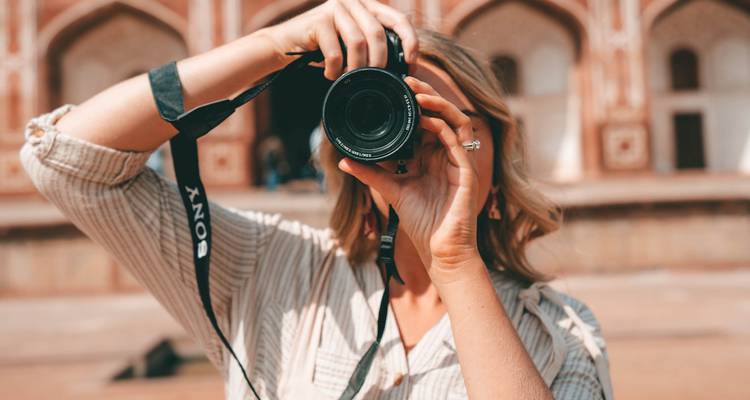 Persona tomando una fotografía con una estructura histórica al fondo.