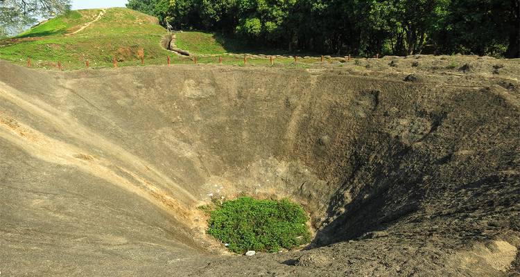 Large crater in the ground surrounded by green vegetation.