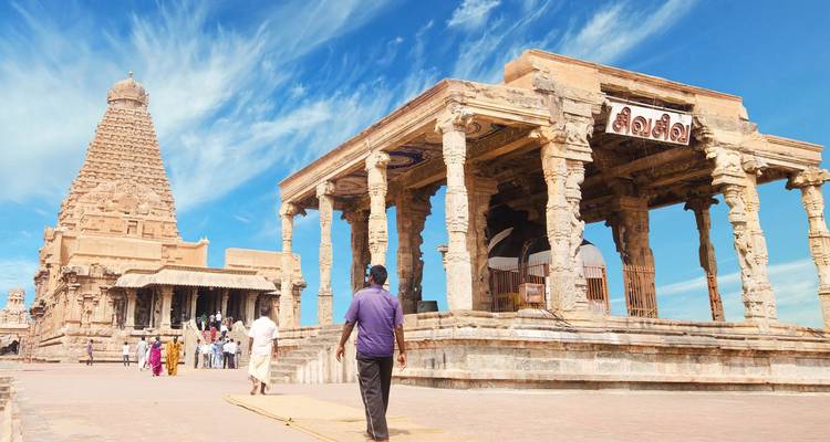 Bezoekers die de sierlijke stenen zuilen en imposante vimana van de Brihadeeswarar Temple onder een blauwe hemel verkennen