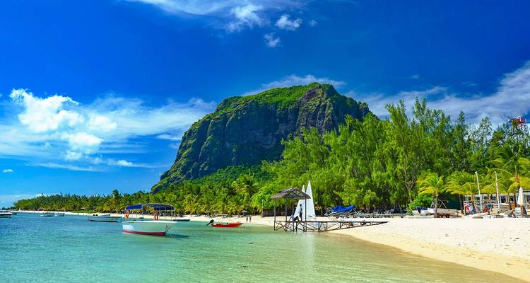 Een turquoise lagune klotst tegen een witgeel strand omzoomd door groene palmen met de indrukwekkend opdoemende berg Le Morne Brabant