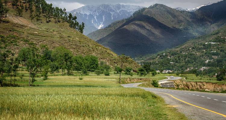 Route panoramique serpentant à travers des collines verdoyantes avec des montagnes en arrière-plan.
