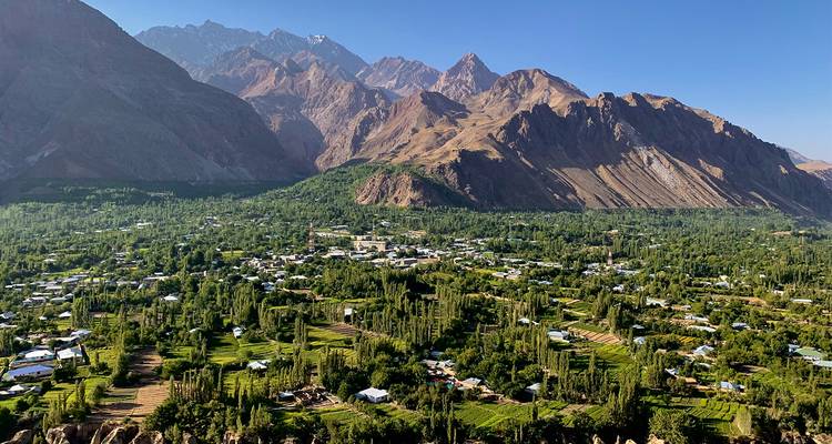 Vue panoramique d'une vallée avec un arrière-plan montagneux et des maisons dispersées.