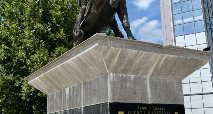 Une statue d'une figure à cheval sur un piédestal avec des bâtiments modernes en arrière-plan.