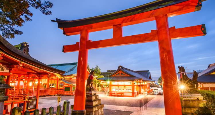 Portail torii orange vif au sanctuaire Fushimi Inari brillant au crépuscule avec les bâtiments du sanctuaire en arrière-plan