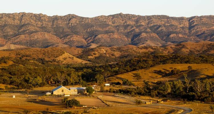 Een landelijk landschap met bergen en een boerderij op de voorgrond.