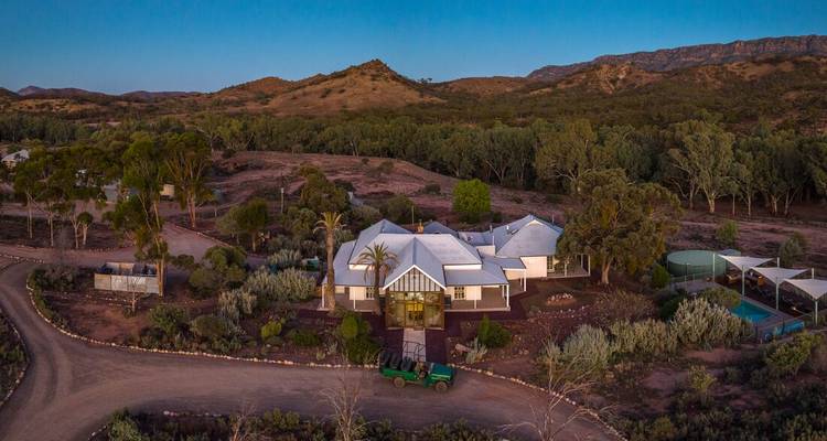 Een groot landgoed met een modern huis omringd door bergen bij zonsondergang.