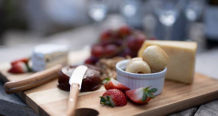 Un gros plan d'un plateau de fromages et fruits en extérieur, légèrement flou.