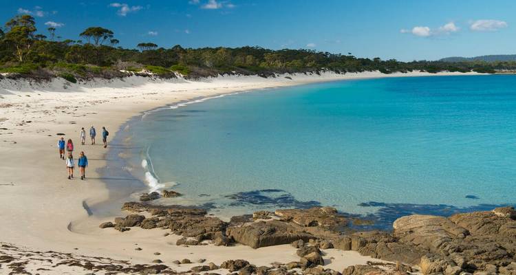 Groupe marchant le long d'une longue plage de sable incurvée avec de l'eau turquoise.