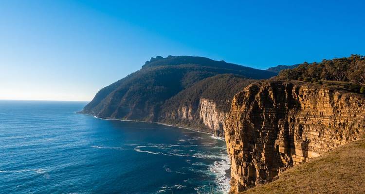 Falaises spectaculaires surplombant un vaste océan avec des vagues qui se brisent.