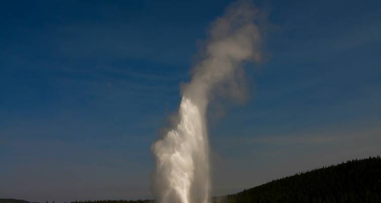 Geyser en éruption avec un ciel bleu dégagé.