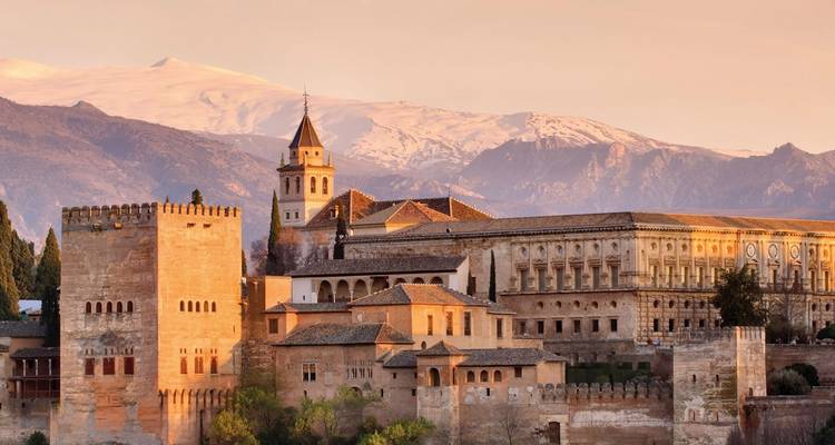 Sonnendurchflutete Aussicht auf den Palastkomplex der Alhambra vor fernen schneebedeckten Bergen während der goldenen Stunde.