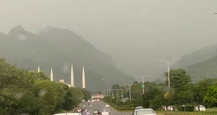 Ein malerischer Straßenblick mit Bergen und der Faisal-Moschee in der Ferne.