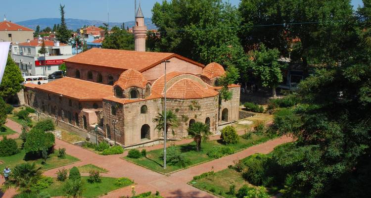 Historische moskee met rood betegeld dak omgeven door weelderig groen.