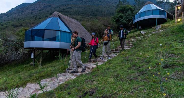 Groep wandelaars die over een stenen pad lopen langs moderne hutten.