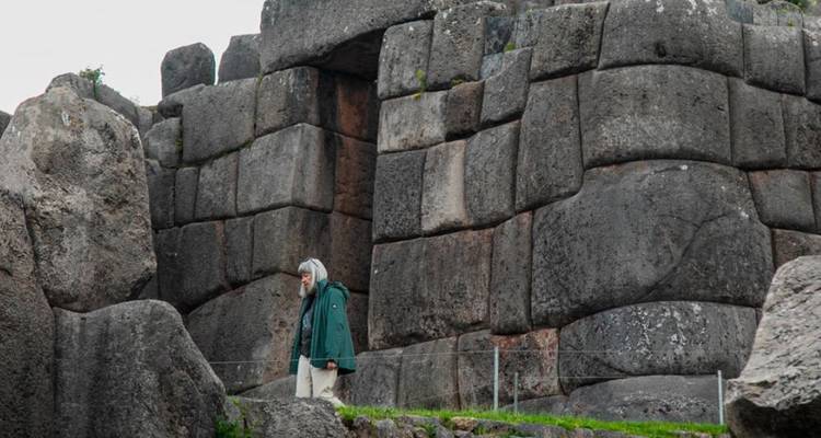Persoon in een groene jas lopend tussen oude stenen ruïnes.