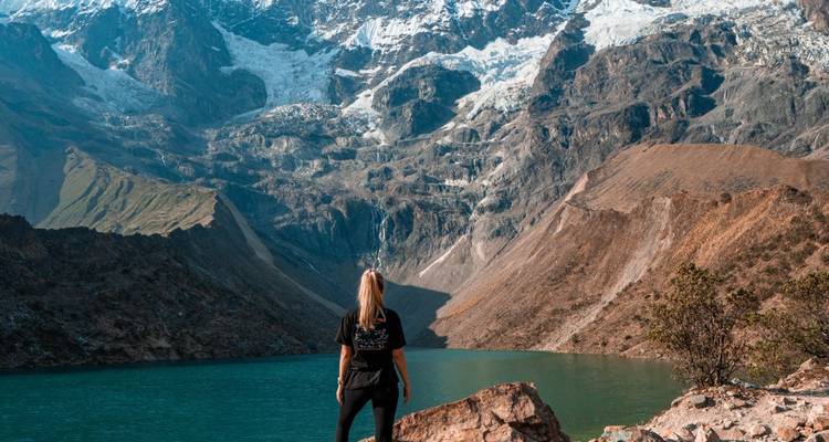 Persoon die een bergzicht bij een meer bewondert, omringd door besneeuwde toppen.