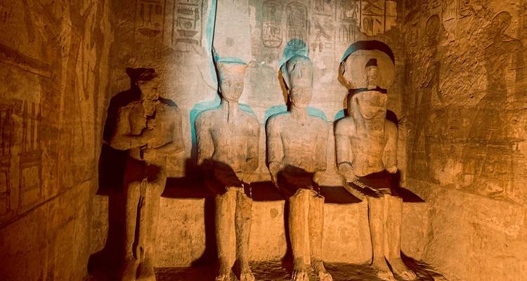 Intérieur d'Abou Simbel avec des statues de pierre illuminées par une lumière chaude.
