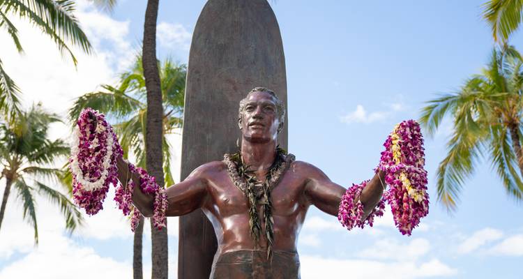 Statue ornée de colliers de fleurs, entourée de palmiers.