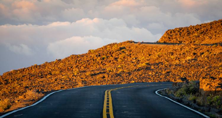 Route ouverte traversant un paysage rocheux et aride sous un ciel nuageux.
