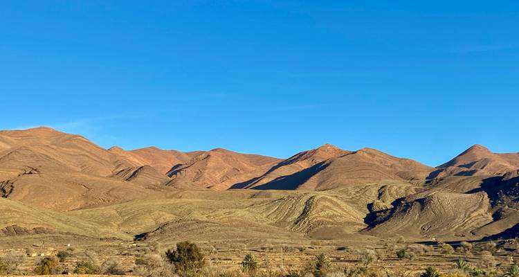 Dorre landschap met glooiende heuvels en heldere blauwe lucht.