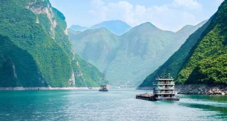 Ships navigating through a river flanked by green mountains.