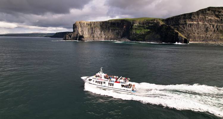 Un bateau de tourisme passe rapidement devant les majestueuses Falaises de Moher sous un ciel dramatique.