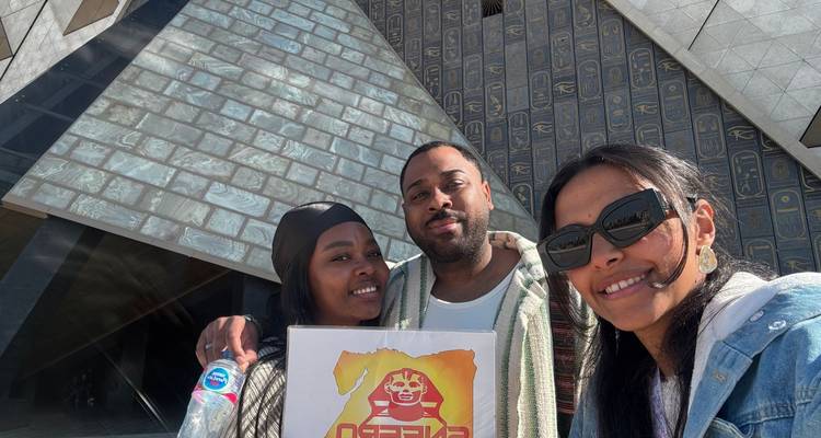 Drie mensen poseren met een bord voor een piramide-ingang.