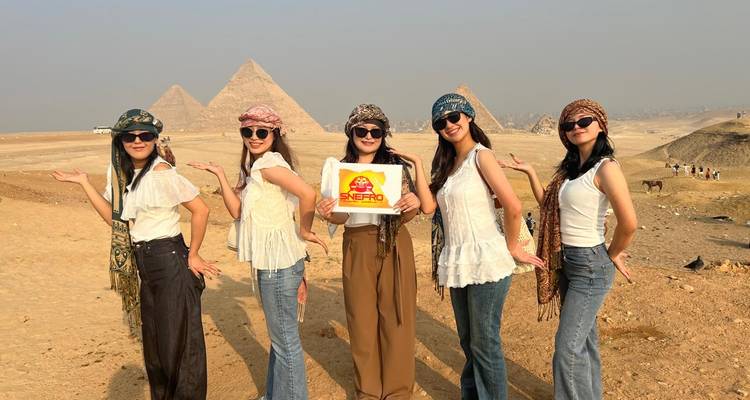 Vijf vrouwen poseren met een bord voor piramides.