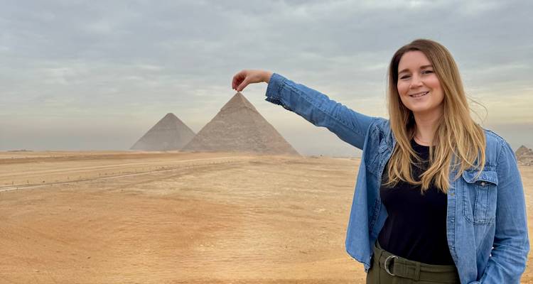 Mujer posando de manera juguetona con dos pirámides famosas al fondo.