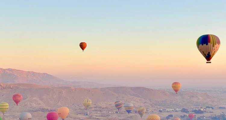 Globos aerostáticos flotando sobre un área desértica al atardecer.
