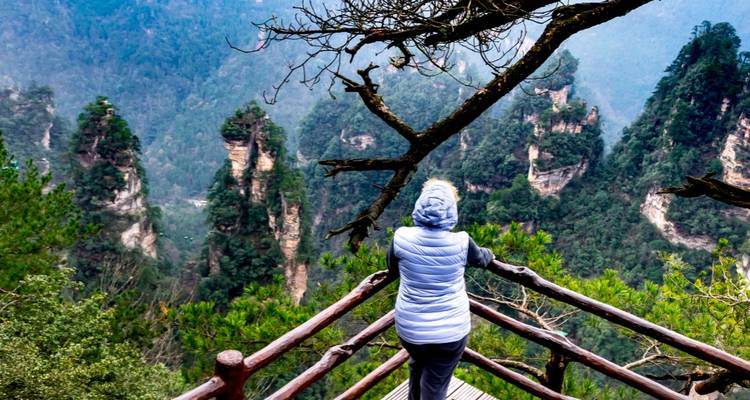 Persoon gewikkeld in jas kijkend naar de bergen van Zhangjiajie.