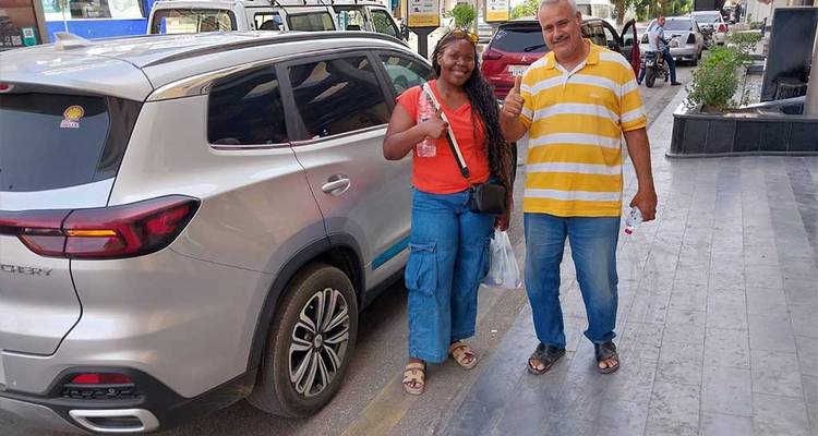 Un touriste et un local debout à côté d'une voiture argentée, souriants.