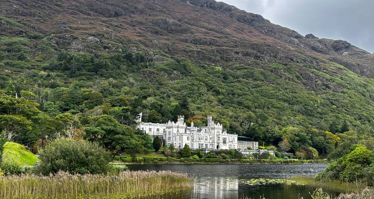 Vue sereine de l'Abbaye de Kylemore reflétée dans son lac avec des montagnes boisées en arrière-plan.