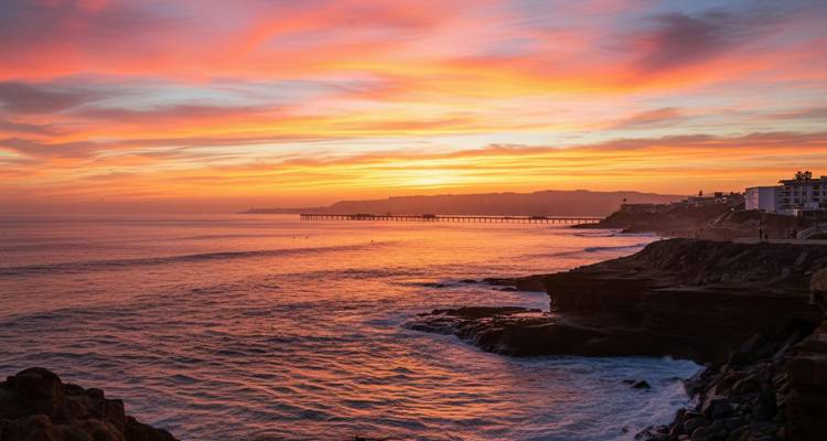 Vue du coucher de soleil sur l'océan avec une jetée au loin et un ciel coloré.