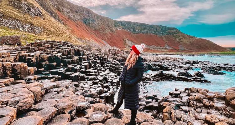 Persona de pie en la Calzada del Gigante con paisaje rocoso y colinas.