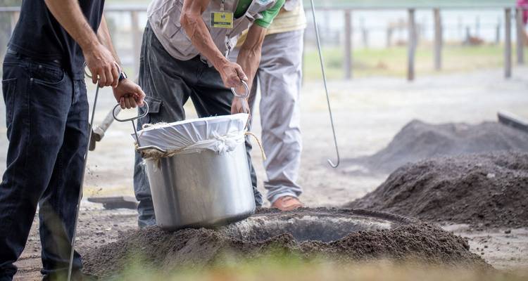 Hommes s'adonnant à la cuisine traditionnelle en enterrant une marmite dans la terre chaude.