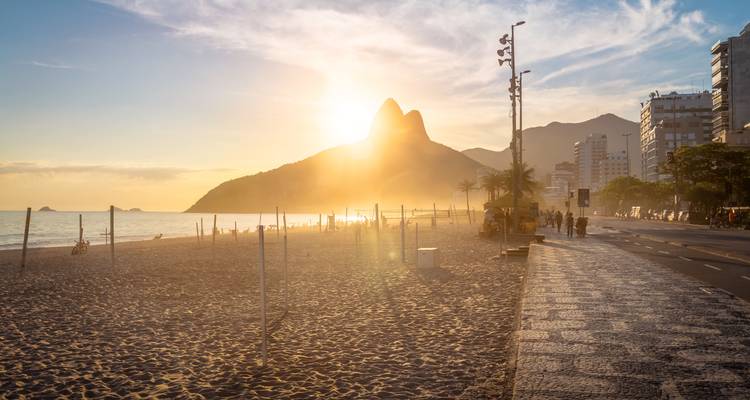 Vue du coucher de soleil d'une plage avec une montagne en arrière-plan, présentant une lueur dorée.