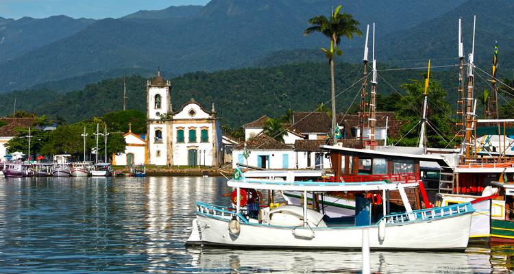 Bateaux ancrés dans un port pittoresque avec des bâtiments coloniaux et des montagnes.