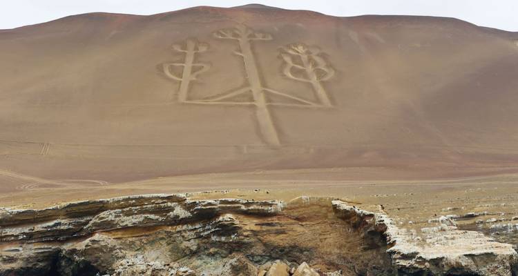 Un geoglifo antiguo y grande en una ladera con terreno rocoso abajo.