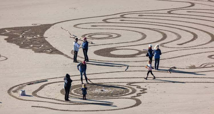 Personas creando diseños elaborados en la arena en una playa.