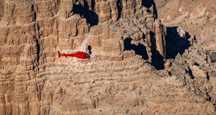 Helicóptero rojo volando junto a acantilados empinados y rocosos.