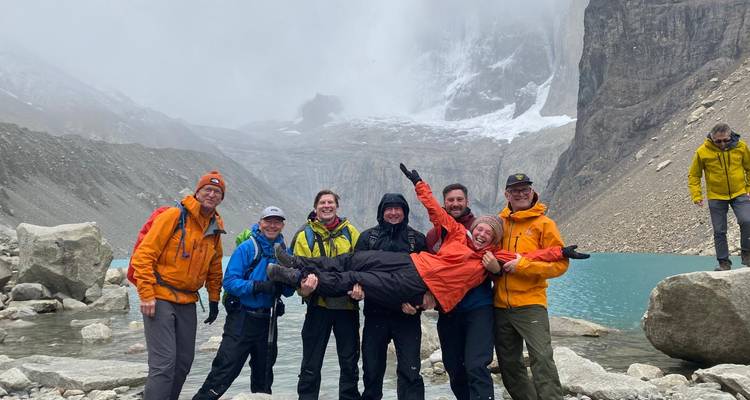 Grupo de senderismo celebra junto a un lago glacial de aguas turquesas bajo imponentes agujas de granito