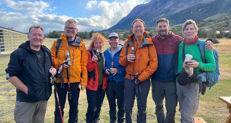 Los excursionistas se relajan tomando bebidas después de la caminata, con las montañas de fondo bajo un cielo parcialmente nublado